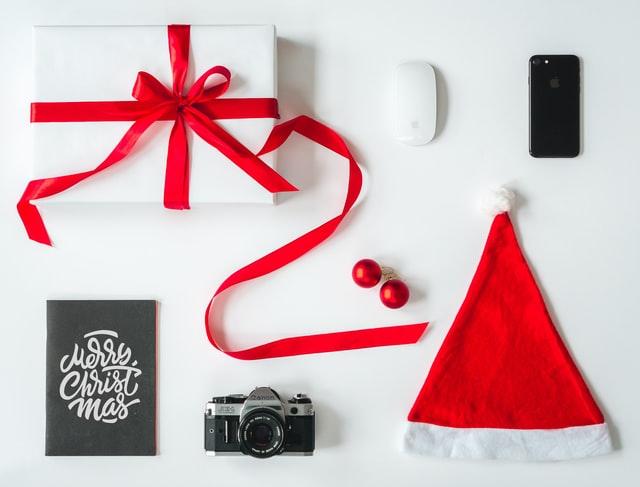 red and white christmas present, a cell phone, computer mouse, camera, christmas card and a red santa hat on a white background